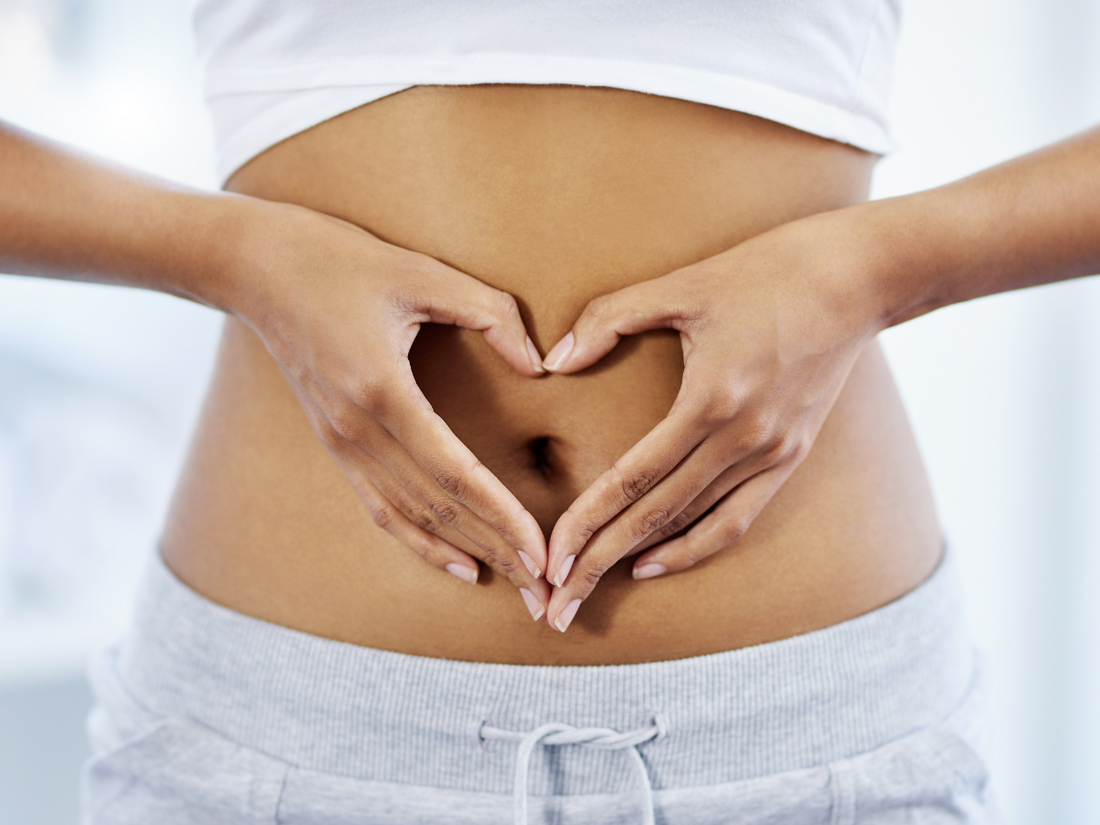 Lady in white outfit with hand clasped in heart shape at the center of her stomach to illustrate a healthy gut