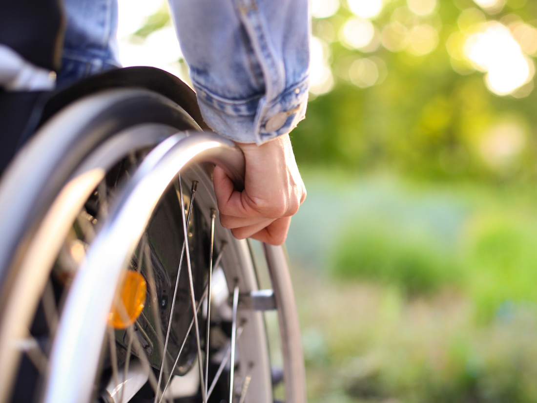 Hand pushing wheels of a wheelchair in outdoor landscape
